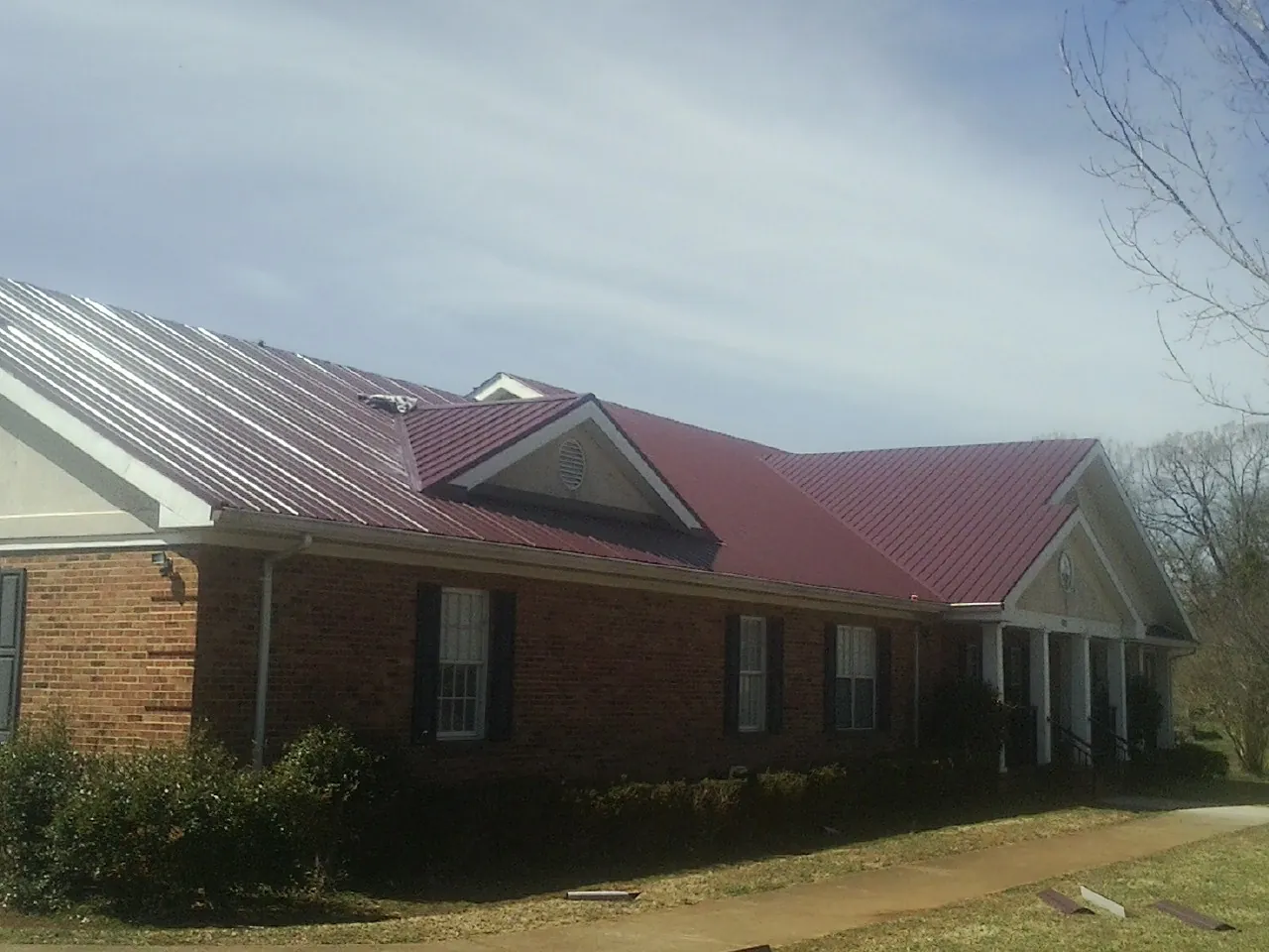 Red metal roof with gabled entries on a long brick building, from a Hail Damage Roof Repair job in Packwood