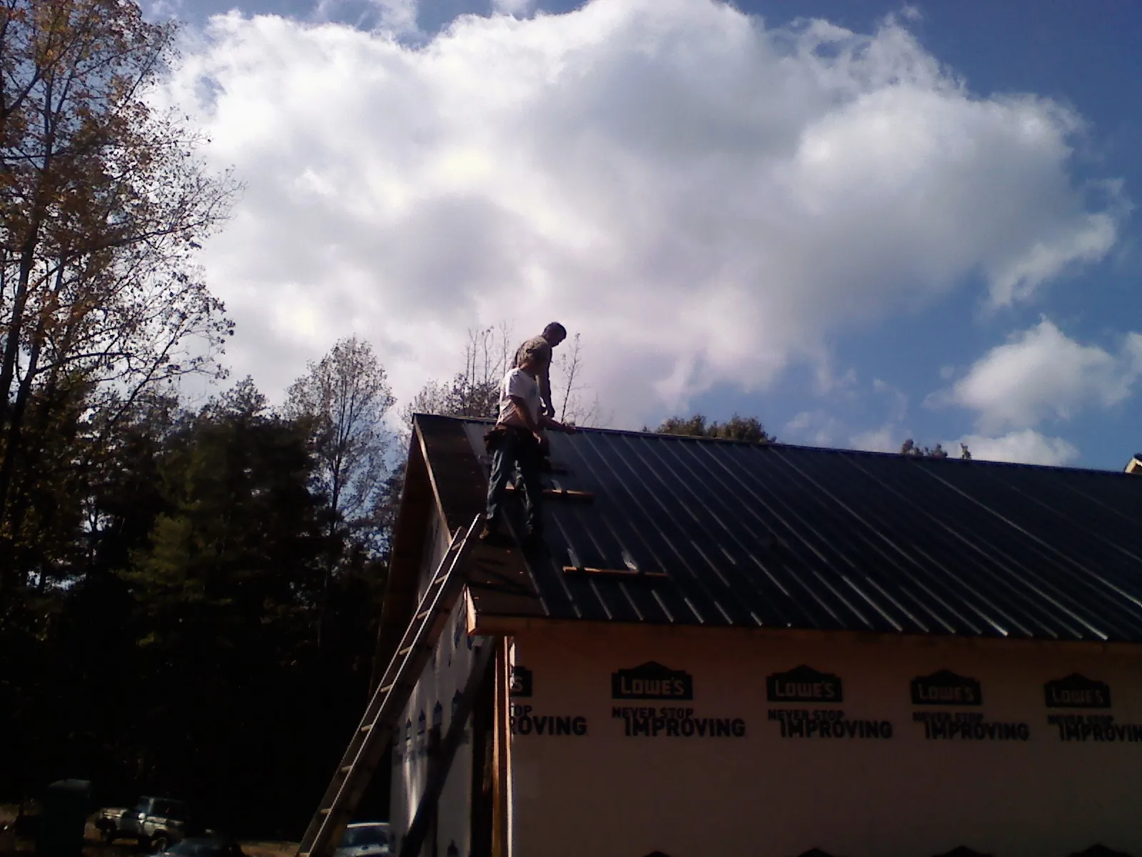 Roofer fastening dark metal panels high against a cloudy sky, from a Roof Inspection job in Packwood