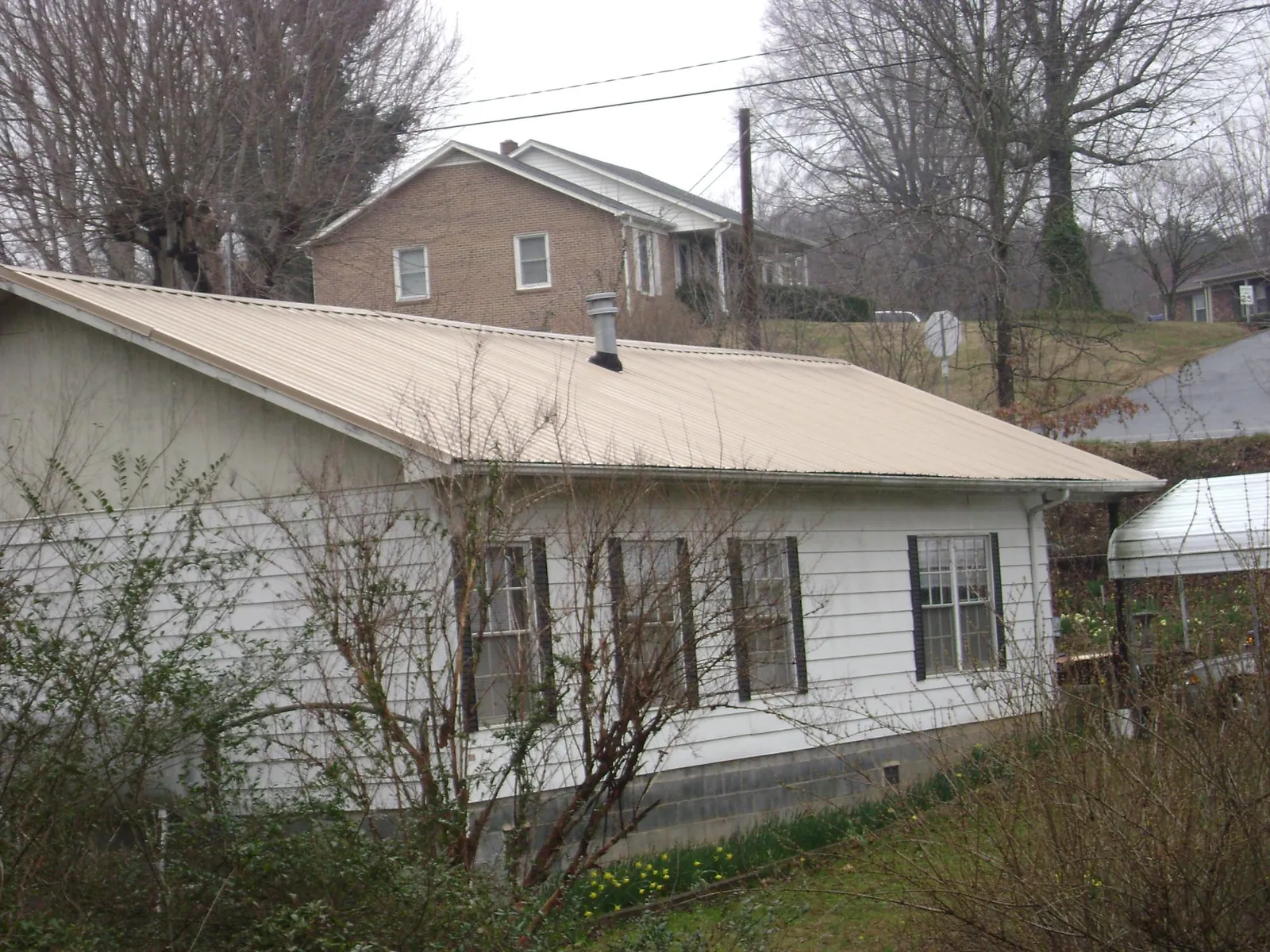 Tan metal roof on a white sided house set into a hillside — Commercial Roofing by Roofing Brothers in Packwood